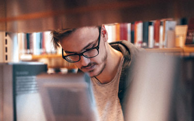 Foto de hombre joven revisando libros entre estantes de biblioteca